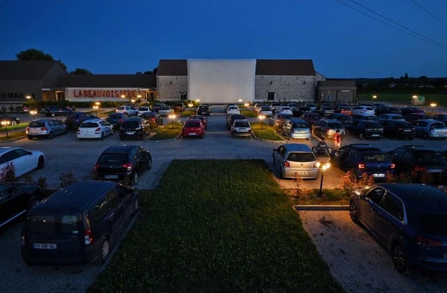 Cinéma drive-in à la tombée de la nuit, avec les véhicules face au grand écran.