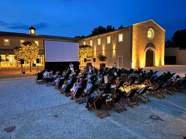 Cinéma en plein air dans une cour éclairée à Oppède, avec écran et rangées de transats.