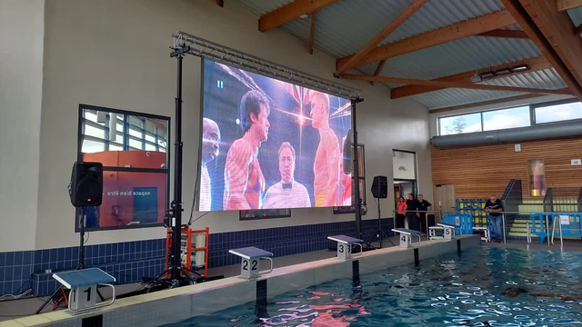 Écran LED installé au bord du bassin dans une piscine intérieure.