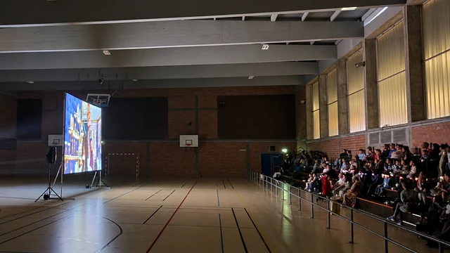 Projection de cinéma dans un gymnase, avec le public installé dans les gradins face au grand écran.