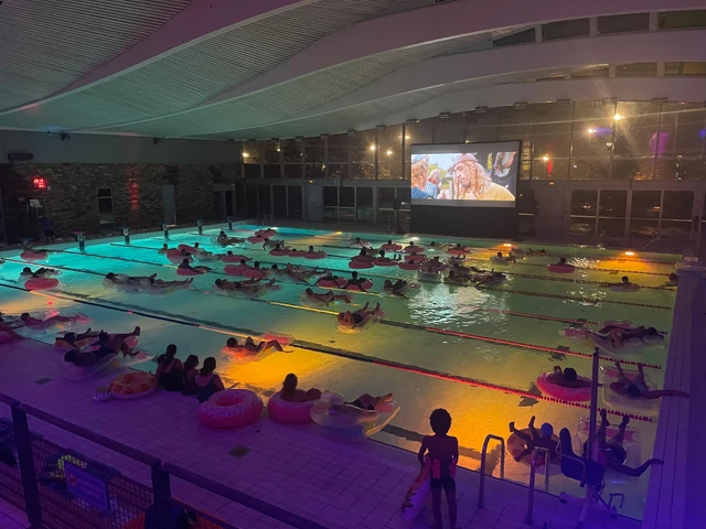 Séance de cinéma piscine avec les spectateurs sur des bouées et des éclairages colorés.